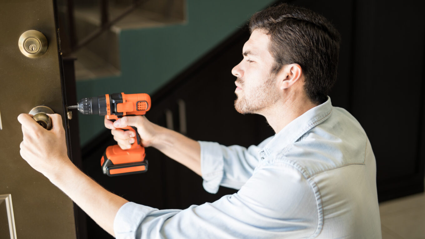profile view attractive handyman using power drill fix door knob house